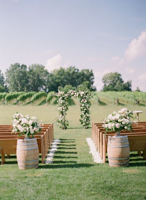 Luxury outdoor wedding at Burning Kiln Winery. Large floral arbour is a showcasing the centre of the ceremony location for a vineyard wedding | Lindsay Plank Events - Niagara and Toronto Wedding Planner. Luxury wedding floral inspiration of white and soft blush pink florals. Wine barrels with lush floral arrangements, with petal rose petals lining the ceremony aisle. Church pews overlook the ceremony location at Burning Kiln Winery for a vineyard ceremony. White and pink floral inspiration. Wine Vineyard Wedding Ceremony, Garden Winery Wedding, Vineyard Wedding Ceremony Decor, Outdoor Wedding Pews, Barrel At Wedding, Large Wedding Flower Arrangements Wine Barrels, Church Pew Outdoor Wedding, Vineyard Wedding Aisle, Vineyard Inspired Wedding