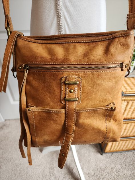 Please review photos for wear and marks. This is a Lucky Brand brown distressed leather crossbody handbag with a slouchy design featuring fringe accents. It has a zip closure, double brown leather handles, and inner pockets. The medium-sized bag is lined with fabric and has a solid pattern. The vintage style is suitable for various occasions such as travel, parties, casual outings, work, or business. It exudes a bohemian, hippie, and cowgirl vibe with a touch of Western and nature themes. Fringe Handbags, Medium Sized Bags, Leather Handbags Crossbody, Bohemian Hippie, Distressed Leather, Leather Handles, Solid Pattern, Leather Handle, Cross Body Handbags