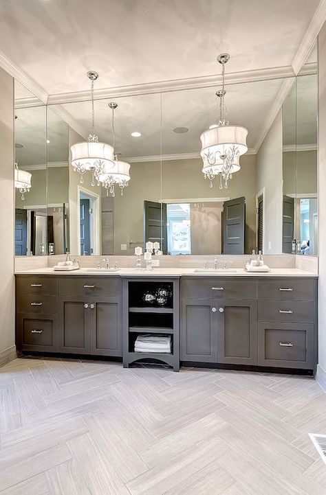 Muted grey vanity with polished nickel pulls and a light stone counter, wraparound mirror, crystal drum chandeliers, light gray herringbone tiled floors: luxury that doesn't seem over the top. Dark Gray Cabinet Bathroom, Gray Herringbone Tile Floor, Gray Herringbone Tile, Herringbone Tile Floors, Casa Clean, Double Sinks, Bathroom Remodels, Master Bath Remodel, 아파트 인테리어