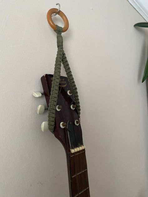 Green guitar or ukulele hanger, ukulele hook, music home decor, ukulele strap, ukulele wall mount, ukulele accessories Wall hanging instrument storage hook made from avocado green recycled cotton on a repurposed wooden hanging ring.  Instrument not included.  One universal size, total length from ring to bottom of loop is approximately 30cm. This simple hanging loop will fit multiple types of string instrument including guitars and ukuleles, but custom orders to fit your specific measurements or Crochet Ukulele Hanger, Guitar And Ukulele On Wall, Macrame Ukulele Hanger Tutorial, Crochet Ukulele Strap, How To Hang Guitars On The Wall, Guitar Holder Wall Diy, Guitar Hanging On Wall, Guitar Hanger Ideas, Crochet Ukulele