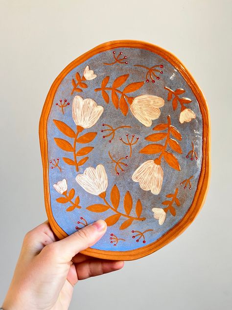 - One of a kind unique handbuilt ceramic serving plate featuring modern folk-style sgraffito design with white flowers. - Beautifully glazed with colorful underglazes and food-safe transparent glaze. - Features tiny berries and folk-style white florals carved in sgraffito technique. - Fired in a kiln twice. MADE TO ORDER - This item would take 4 weeks to make before the order can be shipped. This listing is for a one of a kind ceramic serving plate with a composition of a folk-style design creat Paint Your Own Pottery Spoon Rest, Ceramic Plate Carving, Runny Glaze Pottery, High Fire Ceramics, Ceramic Trimming Designs, Portuguese Pottery Ceramics, Sgraffito With Underglaze, Pottery Catch All Dish, Handmade Plates Pottery