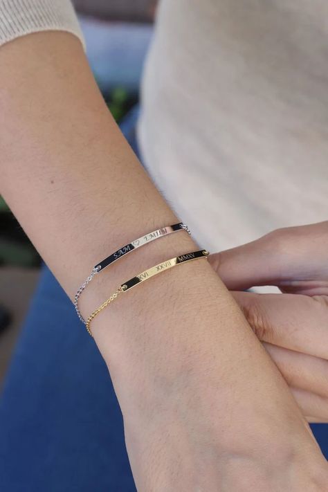 Close-up of a wrist wearing two engraved bar bracelets, one in silver with 'SAM ♥ EMILY' and one in gold with a Roman numeral date, paired with a light sweater and blue jeans. Katie Aesthetic, Bar Bracelet Personalized, Silver Bar Bracelet, Lingot D'or, Nameplate Bracelet, Gold Bar Bracelet, Coordinates Bracelet, Rose Gold Bar, Mom Wedding Gift