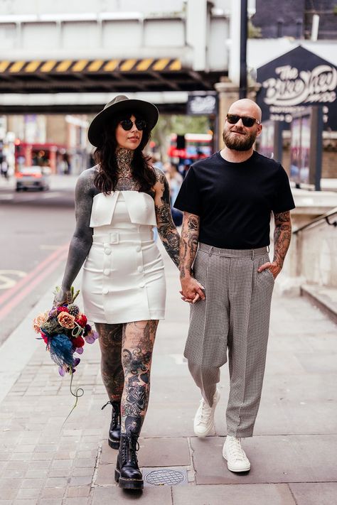 Tattooed bride walks along street wearing short wedding gown, Dr Martens and black hat whilst holding bridal bouquet Wedding Dress With Black, Mother Of The Bride Inspiration, Comic Book Wedding, Hat Inspiration, Short Wedding Gowns, Edgy Wedding, Short Wedding Dresses, Wedding Dresses High Low, Colored Wedding Dress