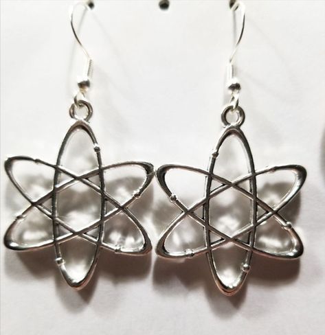 These are a pair of earrings with atomic model charms. They are on a standard ear hook. Atomic Model, Model Earrings, Science Stem, Ear Hook, Atom, Chemistry, Physics, Silver Necklace, Charms