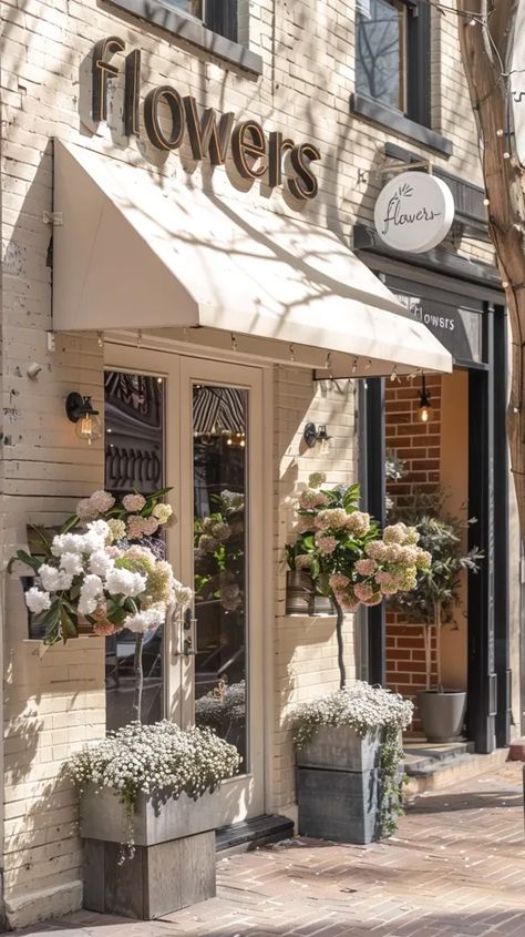 The image shows a flower shop with a cream-colored awning and a brick exterior. The door to the shop is made of glass and there are two large planters with flowers on either side of the door ->> more details in ai-img-gen.com Flower Shop Exterior, Planters With Flowers, Brick Exterior, Coffee Flower, Metal Planters, Shop Front, Floral Shop, Garden Buildings, Large Planters