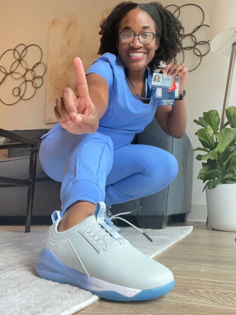 Woman in blue scrubs. She is crouched down with her matching blue shoes extended out towards the camera. She’s holding up her hospital ID badge that reads “resident doctor” in her left hand. And in her right hand she’s holding up a single finger to represent the number 1. Medical Intern, Three Million, Sandra Lee, Medical Doctor, Discovery Channel, White Coat, Doctor Medical, Medical, White