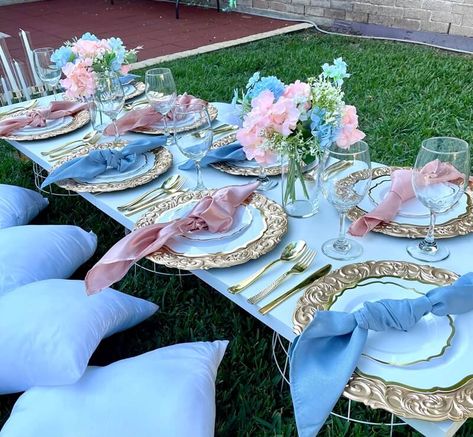 Set up a fabulous tablescape at your garden party with glamorous decorations. Spread a grass rug and place a few cushions alongside your low-height table. Display pink & sky blue hydrangeas along with white baby breaths in clear glass vases placed on the table to add a refreshing vibe to the decor. Glam up the place setting with gold chargers, gold scalloped rim plates, gold cutlery, and pink & sky blue napkins for an eye-catching tabletop decor. Pink White And Blue Party Decorations, Blue And Pink Table Decor, Pink And Blue Party Decor, Pink Blue Birthday Party, Pink And Blue Decor Party, Pink And Blue Tea Party, Blue And Pink Table Setting, Princess Table Setting, Baby Blue And Pink Wedding