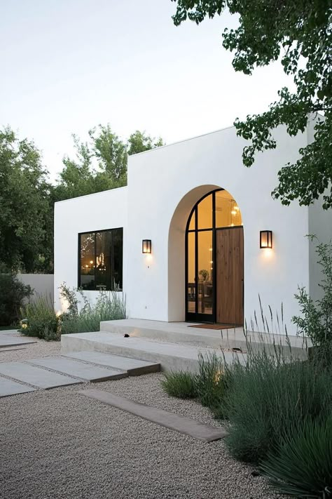 Modern spanish house in white stucco modern arched windows in black trim large handcrafted wooden front door modern lamp fixtures gravel yard with. Unveil the charm and elegance of Spanish houses, and find out how their timeless beauty can inspire your home design. Arch Garage Doors House, Desert Houses Architecture, Stucco Exterior Before And After, Modern Spanish Garden, Transitional Architecture Exterior, Modern Hacienda Exterior, Exterior Arched Windows, Modern Spanish House Interior, Modern Front House Design