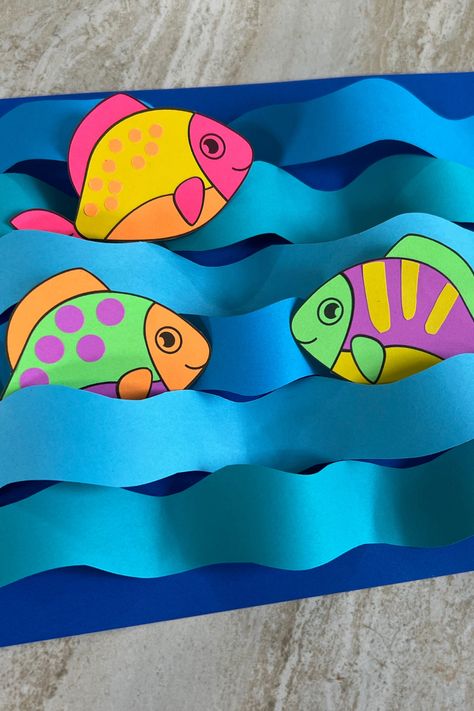 There’s nothing fishy about this craft. To create, download the template and print on your favorite color of Astrobrights paper, or use Astrobrights Bright White to color them yourself!. Cut around the outlines of fish and waves. Alternate the direction of the strips of paper to make the waves. Position your fish and glue. Create your own with our free template! *Difficulty: Easy* Moving Fish Craft, Diy Paper Fish Craft, Paper Waves Diy Crafts, Paper Fish Craft For Kids, Diy Paper Fish, Fish Kindergarten, Fish Crafts For Kids, Paper Fish Craft, Wave Craft