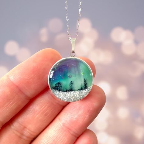 A gorgeous Northern Lights and Aurora Borealis inspired pendant encased in sterling silver round frame.  The pendant showcases the silhouette of tiny trees against a Northern Lights lit night sky and a blanket of snow.  The pendant measures approximately 1.9cm in width and height excluding the bail.   The pendant comes complete with an 18 inch sterling silver chain and is presented in a branded box and wrapped in printed tissue paper.  The back of the pendant is plain pale blue in colour.  Your Northern Lights Wedding Theme, Northern Lights Globe, Northern Lights Jewelry, Northern Lights With Resin, Aurora Borealis Beaded Earrings, Northern Lights Resin Art, Resin Northern Lights, Aurora Borealis Jewelry, Men's Jewelry