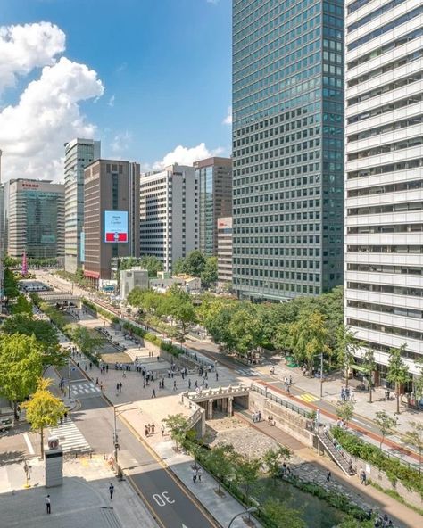 This is a photo of a city street with tall buildings. The image includes tags such as outdoor, cloud, tower block, metropolitan area, commercial building, tree, building, urban area, sky, metropolis, downtown, mixed-use, condominium, urban design, cityscape, skyline, daytime, skyscraper, road, apartment, corporate headquarters, street, tower, and city. Japan Tokyo Wallpaper, Cheonggyecheon Stream, Tokyo Wallpaper, Korea Store, Seoul Attractions, Welcome To Korea, Tree Building, Seoul Korea Travel, Beautiful Blue Sky