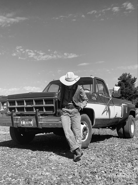 a cowboy is leaning against the front bumper of a vintage gmc truck. the photo is in black and white. they are looking down at the ground, wearing a large hat, a checkered shirt, a vest, and boots. Ranch Photography, Cowboy Photography, Cowboy Ranch, Cowboy Romance, Cowboy Aesthetic, Film Vintage, Wild West Cowboys, Western Life, Spaghetti Western