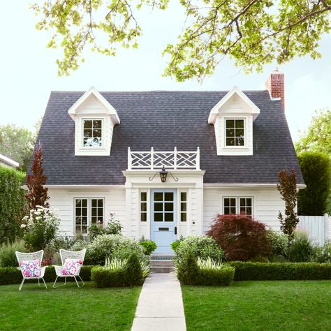 Location: Salt Lake City Built in: 1937 Size: 4,329 sq. ft. Paint colors: (door) Soar and (house) Dover White, Sherwin-Williams “This was an ordinary brick cottage when we moved in — good bones, but not a lot of charm," say homeowners Melissa and Troy Hardy. "Wrapping it in white composite siding and adding a portico breathed new life into it.” They topped their new portico with a pretty mock balcony for over-the-top charm. Green Velvet boxwood tidily envelop a lush mix of plants: iceberg roses, a red-leaf Japanese maple and dawyck purple beech. Cape Cod Entryway Exterior, White Siding Ideas Exterior, Classic White House Exterior, Cottage New Build, Cape Cod House Aesthetic, White House White Trim, Tiny Cottage Exterior, Blue Shutters White House, Cozy Exterior House