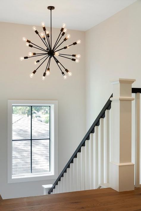 Newell post. An oil rubbed bronze sputnik chandelier illuminates a white staircase accented with a black handrail. White Staircase Black Handrail, Black Entry Chandelier, Small Staircase Chandelier, Stair Landing Chandelier, Black Chandelier Staircase, Chandelier For Stairwell, Staircase Lighting Ideas Chandeliers, Staircase Lighting Fixture, Black Handrail