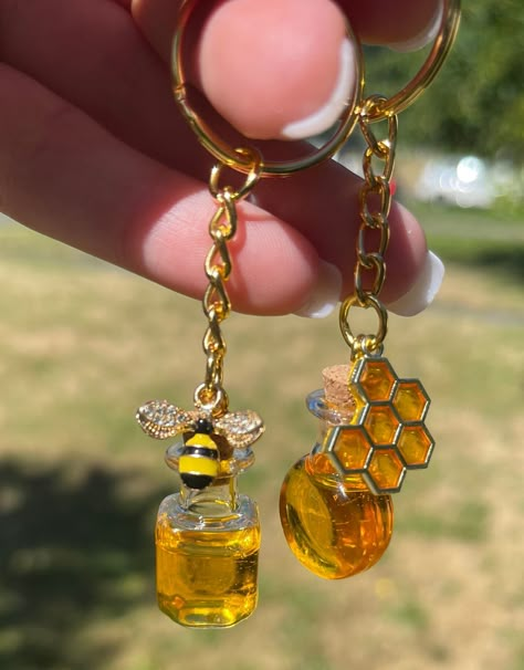 Looking for a sweet way to hold your keys? Check out these resin honey jar keychains, complete with a cute charm on the outside of the jar! 🍯🐝 Perfect for bee lovers and anyone who wants to add a little charm to their day-to-day routine. Plus, each keychain has a unique design that you won't find anywhere else! #resinart #honeycomb #keychains #bees #crafting #DIY #honey #charms #unique #handmade Honey Bee Accessories, Trendy Keychains Resin, Cute Resin Charms, Pendulum Diy, Bee Oc, Bee Gift Ideas, Keychain Inspiration, Honeybee Jewelry, Ashtray Ideas