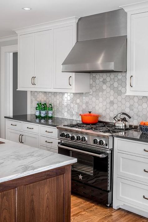 A stainless steel hood mounted against large hexagon marble backsplash tiles is flanked by white shaker cabinets and positioned above a black BlueStar Range located between white cabinets accented with oil rubbed bronze pulls and a charcoal gray quartz countertop. Replacing Kitchen Countertops, Kitchen Countertop Materials, Kabinet Dapur, White Shaker Cabinets, Marble Backsplash, Grey Kitchens, Kitchen Tiles Backsplash, Bath Room, Trendy Kitchen