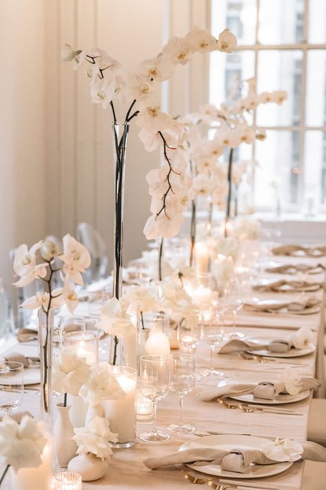 Elegant Luxury Wedding Reception Decor & Table Setup | Immerse yourself in the sophistication of this stunning rooftop wedding at 620 Loft & Garden in Manhattan! This chic wedding reception set up features delicate white orchids in tall, sleek vases, perfectly complemented by soft candlelight. The table is adorned with elegant white tableware and beautifully folded napkins. Perfect inspiration for those dreaming of a classy, intimate New York City wedding with breathtaking views! Orchid Wedding Decor Reception Ideas, Orchids Table Decor, Classy White Wedding Decor, Orchid Table Setting, Timeless Wedding Table Decor, Elegant Classy Wedding Decor, Classy Wedding Decorations, Simple Wedding Centerpieces Long Tables, Modern Wedding Table Settings