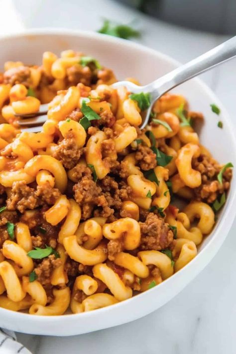 Close-up image of Beefaroni, highlighting the glossy tomato sauce coating the macaroni and ground beef, with specks of Italian seasoning visible, served in a deep dish with a fork on the side, on a simple kitchen tablecloth. Meat Recipes Easy, Meaty Pasta, Cooking Macaroni, Classic Family Meals, Beefaroni Recipe, Easy Quick Dinner, Pasta With Meat Sauce, Beef Pasta, Hamburger Meat Recipes