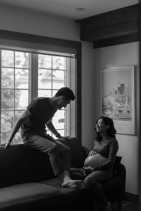 A woman sits on the couch, holding her belly, she looks up at her partner who is sitting on the back of the couch, He smiles down at her. Maternity Shoot In Living Room, Documentary Photography Maternity, Indoors Maternity Shoot, Maternity Photography Documentary, In Home Maternity Photography, Casual At Home Maternity Photos, Chic Maternity Shoot, Documentary Maternity Shoot, Lifestyle Pregnancy Photos