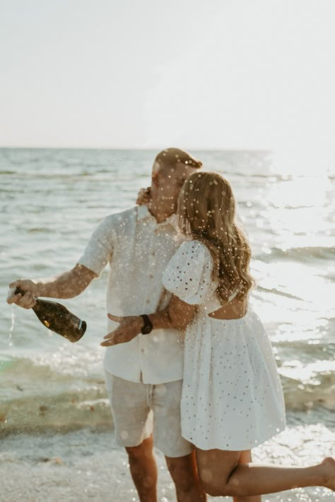 Light And Airy Beach Engagement Photos, Champagne Beach Engagement Pictures, White Dress Beach Engagement Pictures, Beach Engagement Photos Props, Beach Engagement Photos Outfit Men, Champagne Spray Engagement Photo, Engagement Shoot Champagne, Playful Beach Engagement Photos, Beach Engagement Photos Champagne