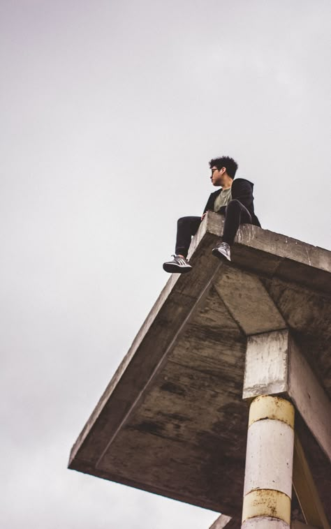 low angle photography of man sitting on ledge during daytime, NIKON CORPORATION, NIKON D5200, #241F1D Man Sitting On Ledge Reference, Sitting Over Ledge Pose, Low Angle Pose Reference Sitting, Sitting On A Ledge Reference, Sitting High Angle Pose Reference, Sitting On Roof Reference, Sitting On Ledge Pose Drawing, Men Poses Sitting, Person Sitting On Ledge Reference