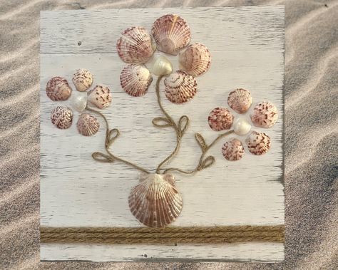 Infuse your space with the essence of the ocean with this exquisite bouquet wall hanging, meticulously crafted from Florida scallop shells. A perfect gift for any occasion, especially for those who cherish the beach! Each piece is a testament to nature's beauty, featuring genuine shells arranged in a simple yet captivating bouquet of daisies. The centers glisten with cream jingle shells, while the petals are fashioned from pink-toned scallop shells. Natural jute stems elegantly support the arran Ideas To Use Seashells, Seahorse Shell Art, Sea Shell Flowers Diy Seashell Crafts, Olive Shells Crafts, Crafts With Clam Shells, Sea Shell Resin Art, Sea Shell Art Diy, Seashell Canvas Art, Sea Shell Crafts Seashell Art