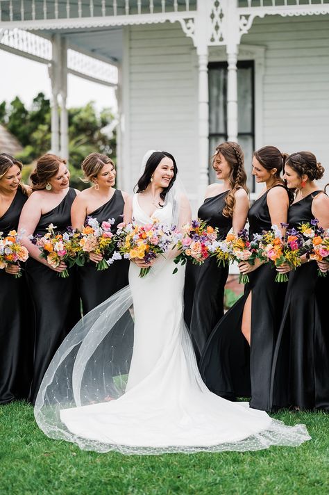 Bride with bridesmaids in black gowns with colorful bouquets Black With Wildflowers Wedding, Black And White Weddings With A Pop Of Color, Black Wedding Bright Flowers, White Wedding Bouquets With Pop Of Color, Black With Bright Colors Wedding, Black Bridesmaid Dresses Colorful Shoes, Summer Wedding Colors With Black, Black Wedding With Bright Flowers, Black And White Wedding With Colored Flowers