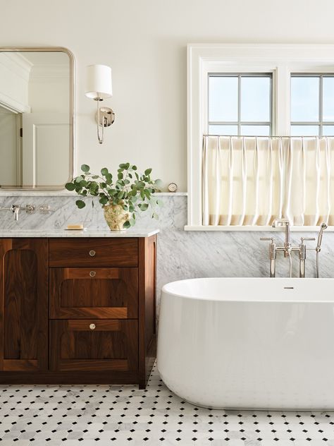 The tranquil primary bath focuses on refined finishes, such as the Carrara marble slab wainscoting and marble mosaic flooring from The Tile Shop. A freestanding Kohler Ceric tub with a wall-mounted Waterworks faucet anchors the space. Waterworks Faucet, Bathroom Wainscoting Ideas, Lannister House, Carrara Marble Bathroom, Brass Shelving, Wainscoting Bathroom, Marble Tile Bathroom, Wall Mount Tub Faucet, Primary Bath