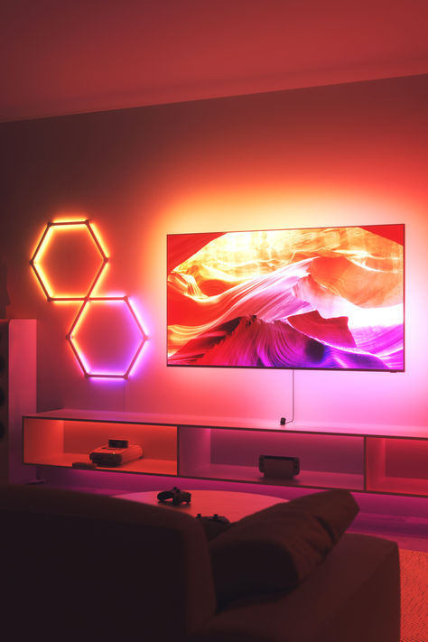 Living room with TV, gaming controllers on coffee table, and glimpse of couch, illuminated by Nanoleaf 4D and Lines in red, orange, and purple hues, synced for immersive gaming experience. Tv Astethic, Console Gaming Setup, Tv Led Lights, Nanoleaf Lines, Mirror Camera, Line Tv, Console Gaming, Movie Theatre, Screen Mirroring