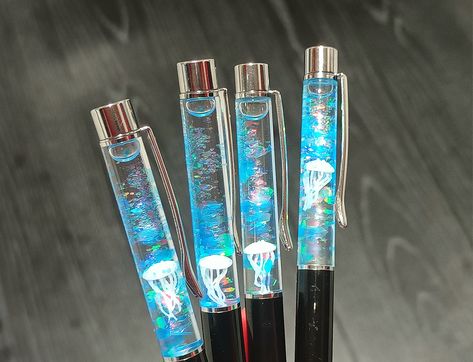 These stunning, floating ballpoint pens encapsulate a tiny jellyfish, chunky glitter and tiny glass bubbles ~ they make super unique gifts for loved ones. The contents are sealed inside the top part of the pen to prevent leakage. The pen can be opened and close by twisting the nib. 🦑 Dimensions: 10mm (W) x 140mm (L) 🖤 Ink Colour: Black 🦑 Worldwide shipping 🖤 FREE UK delivery Cool Pens, Gel Pen Aesthetic, Floating Liquid Keychain, Floating Glitter Pens, Jellyfish In Water Bottle, Unique Stationary, Olympus Pen, Unique Pens, Cute Pens