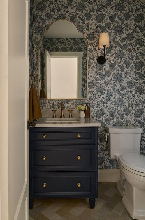 Powder room features a navy blue washstand with marble countertop and antique brass vintage style faucet under a silver leaf arch mirror mounted on white and blue botanical wallpaper. Navy Blue Powder Room, Grey Trellis Wallpaper, Blue Botanical Wallpaper, Blue Powder Room, Blue Velvet Couch, Wainscoting Bathroom, White Shutters, Blue Floral Wallpaper, Changing Table Dresser