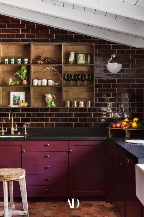 The actor and her designer opted for a darker, moodier kitchen rather than an all-white space. Aubergine wall tile by Waterworks, 19th-century terra-cotta floor tiles by Chateau Domingue, majolica backsplash and marble by Compas Stone, a cubby shelf from Nickey Kehoe, and a Pierre Jeanneret stool from Galerie Half all fill the cozy cooking space. #beams #subwaytiles #barstools #barstool #countertop #sink #beams #openshelving #cozy #kitchen #cooking #ranchhouse #ranchhome #faucet #vases #lighting Kirsten Dunst Kitchen, Kirsten Dunst Home, Kirsten Dunst House, Dark Purple Cabinets, Moody Kitchen Decor, Moody Kitchen Ideas, Moody Kitchen Design, Moody Spaces, Moody Room