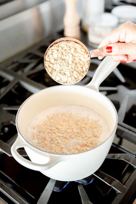 Hand holding copper measuring cup dumping dry oats into water and milk mixture in a white ceramic coated pot on the stove. Oatmeal On The Stove, Rolled Oats Recipe, Oats With Milk, Protein Porridge, How To Make Porridge, Make Oatmeal, Savory Oatmeal, Cooking Oatmeal, Protein Oatmeal