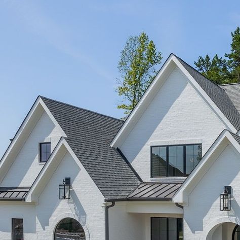 LINNANE HOMES | Custom Home Builder Charlotte, NC on Instagram: "This elegant two-story home features a classic white brick exterior complemented by a dark gray shingled roof. Its design boasts multiple gables and large, black-framed windows that enhance the home’s modern aesthetic. The front entrance is marked by a charming arched doorway, leading to a small set of stairs. The property is beautifully landscaped with well-maintained shrubs and pathways, creating a welcoming and sophisticated curb appeal. Surrounded by lush greenery and trees, this home offers both style and tranquillity.  ✅VOTE FOR US!🙌 Charlotte’s Best - Homebuilder!  ➡️LINK IN BIO _______________________________________________ Did you know that we have several home lots available at Twin Lakes in Weddington, North Caro Roof Gables Ideas, White Brick Exterior, Shingled Roof, Framed Windows, Arched Doorway, Gorgeous Homes, Arch Doorway, Brick Exterior, Twin Lakes