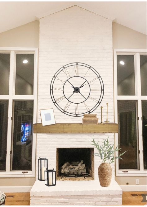 Cream floor to ceiling fireplace with natural mantle, large clock, candlesticks, on hearth is a lantern and woven vase with faux stems Wall Clock Over Fireplace Mantles, Clock Above Fireplace Mantels, Fireplace Mantle Decor With Large Clock, Clock Over Mantle Fireplaces, Large Clock Above Fireplace, Fireplace With Clock Above, Clock On Mantle Fireplaces, Large Clock Over Fireplace, Fireplace Mantle Decor With Clock