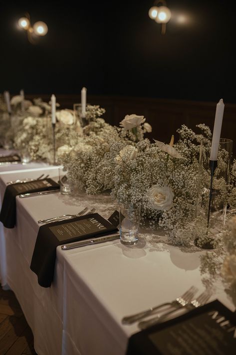 To bring their modern Art Deco reception to life, the bride and groom chose timeless black and white elements, as well as clear architectural details including their seating chart with white printed lettering in a variety of contemporary fonts. Black and white linens were adorned with trendy baby's breath centerpieces accented by full white roses. #weddingdecor #weddingideas #babysbreath December Wedding Black And White, Trendy Wedding Centerpieces, Black And White Wedding Dinner, Black White And Beige Wedding Decor, White Wedding Black Accents, Black And White Bride And Groom, Black Tie Wedding Reception Centerpieces, Black White Wedding Centerpieces, No Flower Centerpieces Wedding