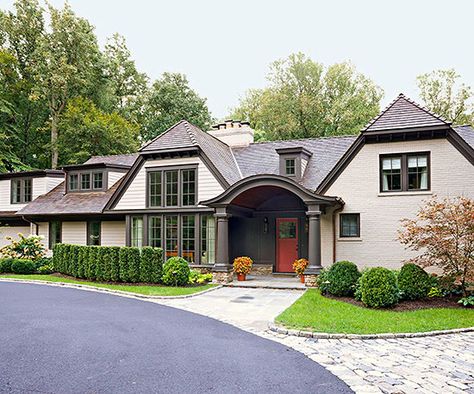 A renovation inspired by English country house design graced this exterior with abundant charm. The addition of dormers and gables, chocolate-brown trim, a cedar-shingle roof, and painted brick distinguish the home with cottagelike character; even the granite cobbles edging the path to the columned front entry evoke storybook appeal. Colors For House, Paint Colors For House, Tan House, Ranch House Remodel, Best Exterior Paint, Dark Trim, Brown Roof, Country House Design, Exterior Color Schemes