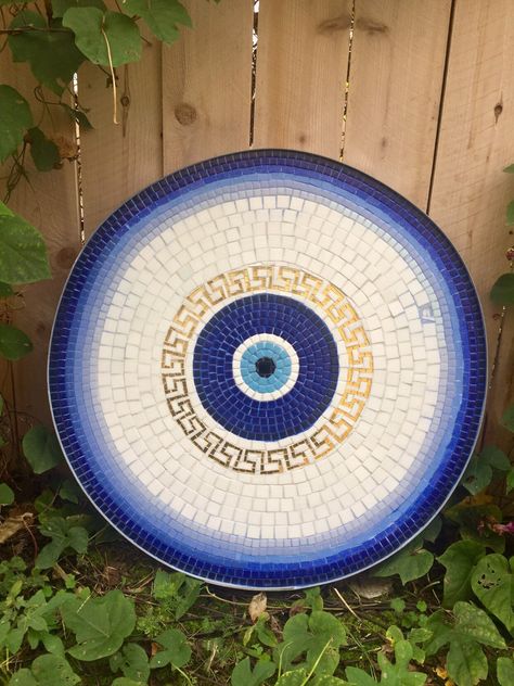 These mosaic bistro tables are handmade with cut glass using my unique pattern of Greek key and lucky eye on background of blue and white. These handmade table tops can be used as side tables, coffee tables, patio tables or can fit onto any other other table you have and they range in size between 22 and 26 inches. The outer rim is a wine barrel hoop, Inset with a custom cut waterproof cement board. They're weatherproof enough to go outside and stain proof and they make great gifts or additions Mosaic Top Table, Mosaic Bistro Table, Mosaic Round Table Top, Mosaic Table Top Designs Patterns, Greek Decor Outdoor, Mosaic Table Top Diy Outdoor, Mosaic Stump, Round Mosaic Patterns, Round Table Painting Ideas