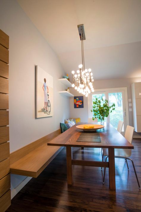 A floating bench built into the wall creates unique seating along the wood dining table. Wall art adds color and decoration while keeping with a polished, minimalist look. A contemporary light fixture features a metal form with small circular bulbs joining with the natural light from the french doors to brighten the space. Floating Banquette Seating, Wall Bench Seating, Long Wood Table, Midcentury Dining Room, Bench Seat Dining, Bench Seating Kitchen, Banquette Seating In Kitchen, Wall Bench, Kitchen Banquette