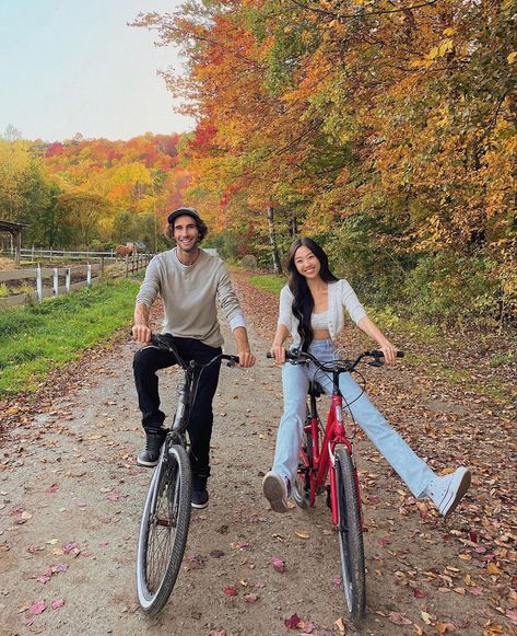 A couple is smiling at the camera as they are riding bikes past trees with orange and yellow leaves. They are enjoying the perfect fall date idea. Couples Riding Bikes, Active Couple Aesthetic, Couple Activities Photos, Biking Date, October Date Ideas, Bike Ride Date, Couple Bike Ride, Active Date Ideas, Cute Fall Date Ideas