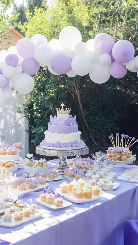 Elegant purple princess-themed birthday setup with tiered crown cake, purple and white balloon garland, and an array of matching cupcakes and treats. Pastel Purple Birthday Theme, Unique First Birthday Ideas, Pastel Balloon Garland, First Birthday Ideas, Party Ideas For Girls, Royal Birthday Party, First Birthday Party Ideas, Princess First Birthday, Purple Princess