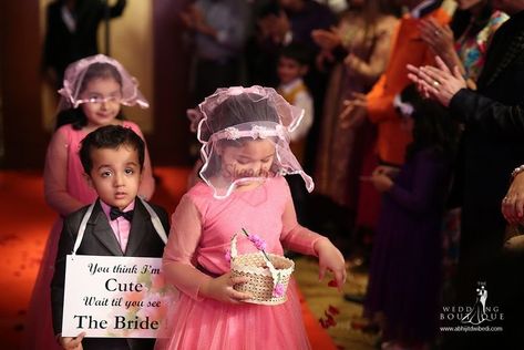 Before you actually walk the aisle, your little munchkins (nieces and nephews) or your squad can hold quirky placards to proceed your entry. It is one sure shot way to add a pinch of curiosity and amp up your bridal entry. So, here we enlist some lovely 'Here comes the bride' photo ideas to load you with inspiration. Groom Entry, Bridal Entry, Bride Entry, Bride Photo, Niece And Nephew, Here Comes The Bride, Flower Girls, Bride Groom, Photo Ideas