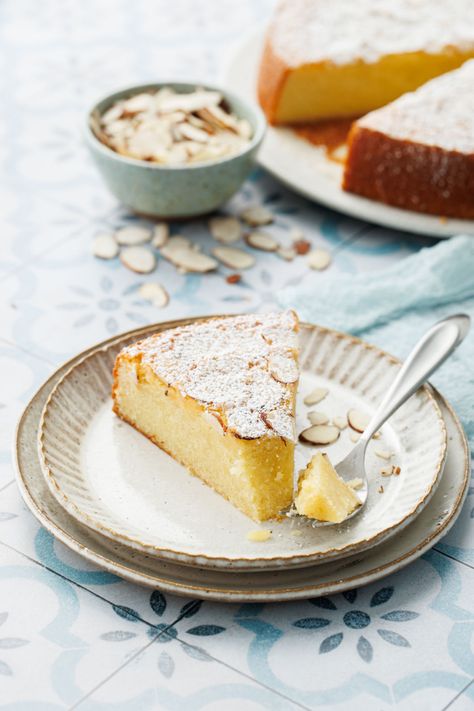 Slice of Flourless Almond Flour Cake on a dessert plate with a bite on a fork, rest of cake and bowl of sliced almonds in the background. German Almond Cake, Flourless Almond Cake, French Almond Cake, Almond Olive Oil Cake, Gluten Free Almond Cake, Almond Torte, Almond Flour Cake, Almond Flour Cakes, Cardamom Cake