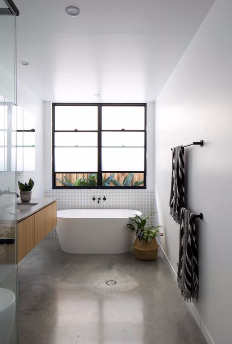 This bathroom uses minimal tiles featuring a burnished concrete floor and only a section of tile behind the bath and vanity splash. Minimalist style black, white and timber bathroom. See all the photos from this home tour on the blog. Burnished Concrete Floor, Concrete Floors Bedroom, Polished Concrete Bathroom, Bathroom Concrete Floor, Burnished Concrete, Style Curator, Matte Black Wall, Bathrooms Ideas, Timber Vanity