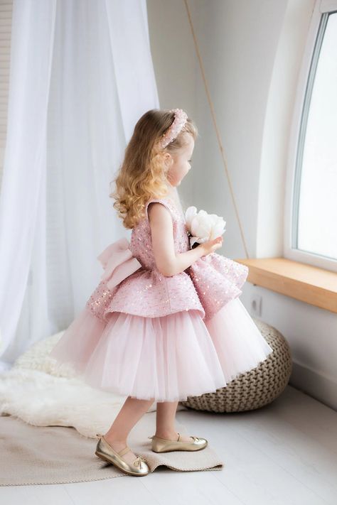 Add a sprinkle of sparkle to your little one's big day with this sequin-adorned tulle flower girl dress from Lily Couture. Perfect for birthdays, pageants, and special occasions, this dress features layers of soft tulle and dazzling sequins, making your child shine. The large bow at the back adds a sweet, elegant touch, while the sleeveless design ensures comfort. Available in blush pink this dress is designed for unforgettable moments and magical memories. Perfect for parents seeking an enchant Dress With Big Flower, Pink Dress Bow, Pink Blush Dress, Pink Pageant Dress, Baby Christening Outfit, Girls Communion Dresses, Tulle Flower Girl Dress, Blush Dress, Flower Girl Crown