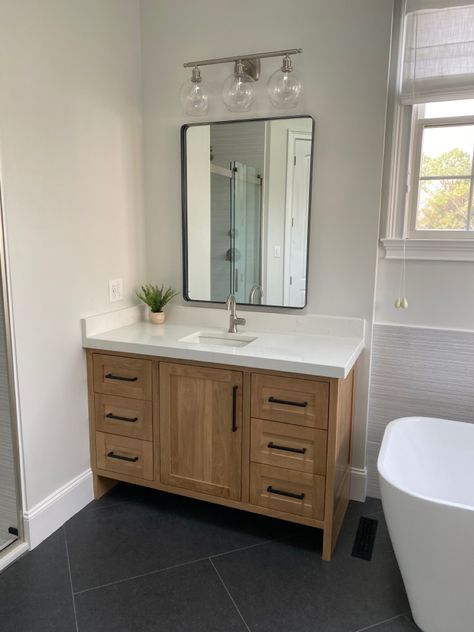 White oak cabinets with bianco aspen quartz. 24x48 tiles in herringbone pattern Oak Wood Vanity Bathroom, White Oak Cabinet Bathroom, Oak Vanity Black Hardware, White Bathroom With Wood Cabinets, Wood Cabinets Master Bath, Bathroom White Oak Cabinets, Natural Wood Bathroom Vanity With Dark Floors, Wood Cabinets White Counter Bathroom, Natural Wood Cabinets Bathroom