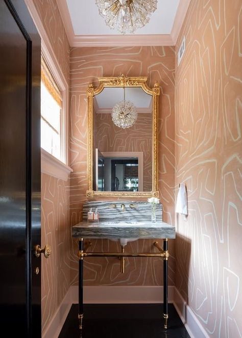 Lined with salmon pink crown moldings and baseboards, walls clad Kelly Wearstler Groundworks Graffito Wallpaper accent a contemporary pink and black powder room boasting a gold French mirror hung over a gray stripe marble sink vanity. Kelly Wearstler Powder Room, Graffito Wallpaper, Grey Powder Room, Light Pink Bedding, Kelly Wearstler Wallpaper, Black Powder Room, Wallpaper Powder Room, Hexagon Floor, Floating Sink