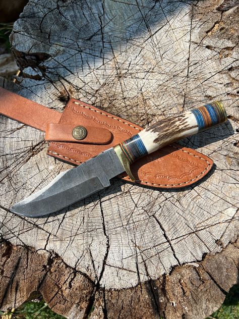 Handmade Damascus Steel hunting knife with stag antler handle and genuine leather sheath, hand-tooled and stitched. Handle length: approximately 4.25" Blade length: approximately 4.75" Overall length: approximately 9" you will receive the exact knife in the photos. All knives are handmade and therefore all unique! Colour, shape, and horn will vary. DISCLAIMER: We are not responsible for any injuries that may occur, so please handle with care! Must be 18+ to purchase. Care Tips: Don't Store your Deer Antler Knife, Scene Setting, Antler Knife, Camping Knots, Knives Hunting, Stag Antlers, Handcrafted Knife, Straight Blade, Leather Ideas