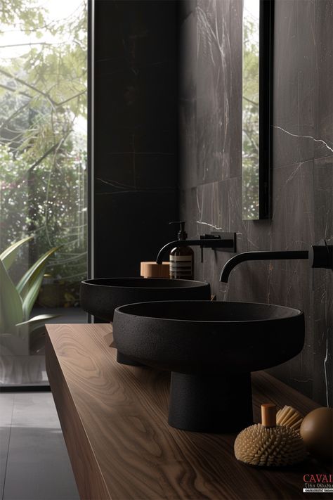 Natural Contrast • Bathroom vanity area highlighted by rich, dark marble back panel • Dual textured matte black basin bowls sit atop a wooden countertop • Wall-mounted matte black faucets offer a modern touch • Natural light streams through the window, creating a serene backdrop • Wooden textures bring warmth to the monochromatic scheme • Thoughtfully placed toiletries and natural brush add a functional yet aesthetic touch • A sleek combination of organic elements and contemporary design. Wood Vanity Black Countertop, Bathroom Dark Aesthetic, Contrast Bathroom, Bathroom Vanity Area, Bathroom Design Wood, Monochromatic Scheme, Black Faucets, Black Faucet Bathroom, Dark Marble