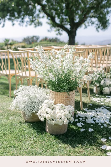 Beginning with wicker baskets of Baby’s Breath, white delphinium and white roses at the start of the aisle, this outdoor wedding at Spanish Hills Club has a serene atmosphere. Wooden chairs and additional floral arrangements carry this theme throughout the ceremony space. The white flowers add a classic touch, complementing the lush green surroundings.   Visit the link for more inspiration on crafting a stunning outdoor ceremony in Los Angeles.   Photo credit: Aura Elizabeth Photography Flowers For Wedding Chairs, Wedding Flower Basket Ideas, White Flowers Down Aisle, Basket Flower Wedding, Beginning Of Aisle Wedding Decor, Wedding Aisle Florals Outdoor, Flowers Ceremony Wedding, Wedding Flower Aisle Arrangements, Wedding Flowers For The Aisle